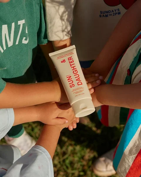 Children holding a tube of Sun & Daughter mineral sunscreen